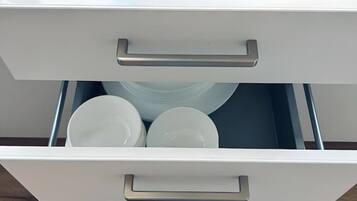 A drawer with white handles containing white plates and a black circular object.