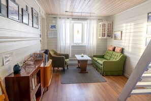 A cozy room with a wooden floor, a green sofa, a small table, and a bookshelf.