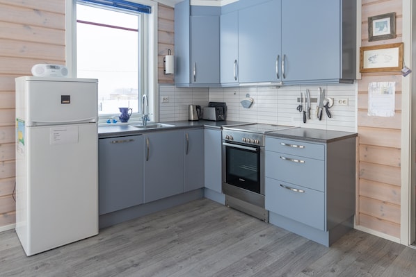 A modern kitchen with light blue cabinets, a built-in oven, and a white refrigerator. - Ekker Island Arctic Lodge (Vadsø)