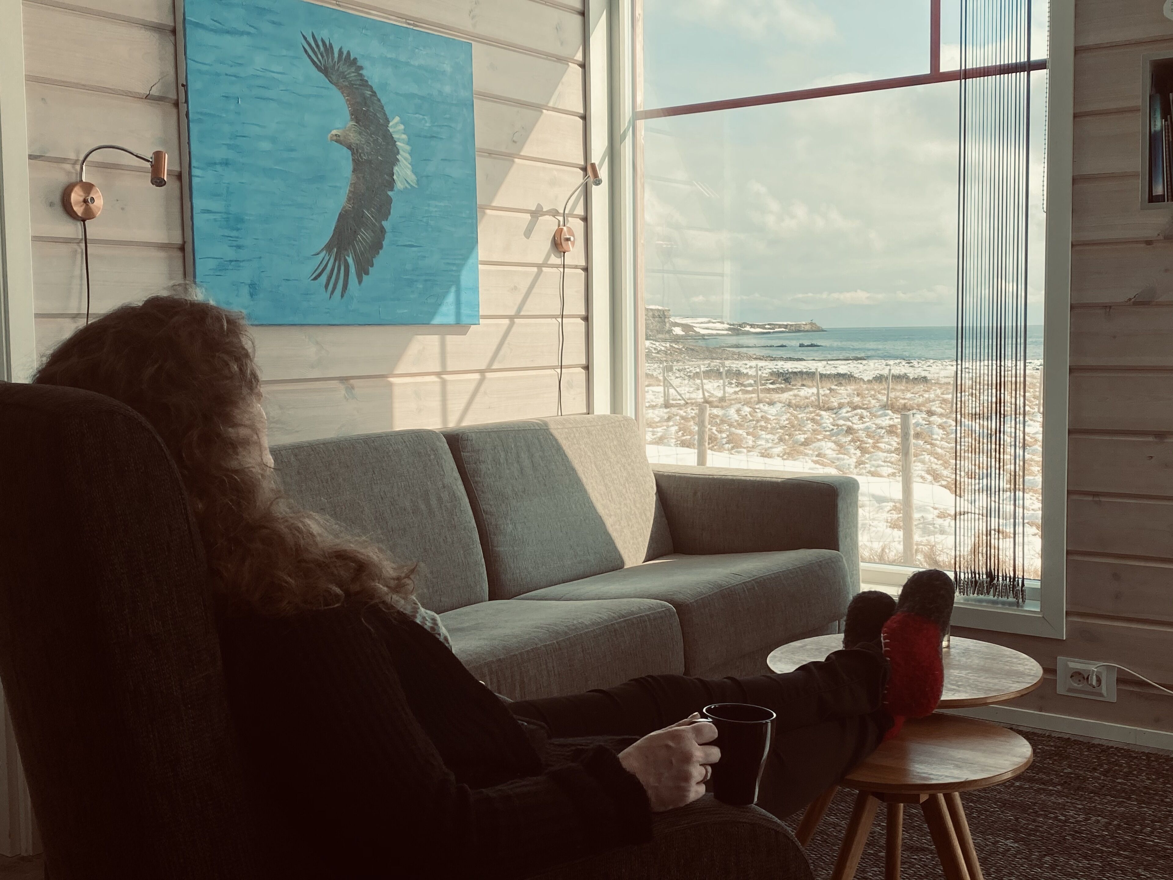 Et værelse med stort vindue, der giver udsigt over en strand og hav.