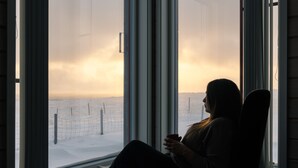 A person seated by a large window with a view of a snowy landscape. - Ekker Island Arctic Lodge (Vadsø)