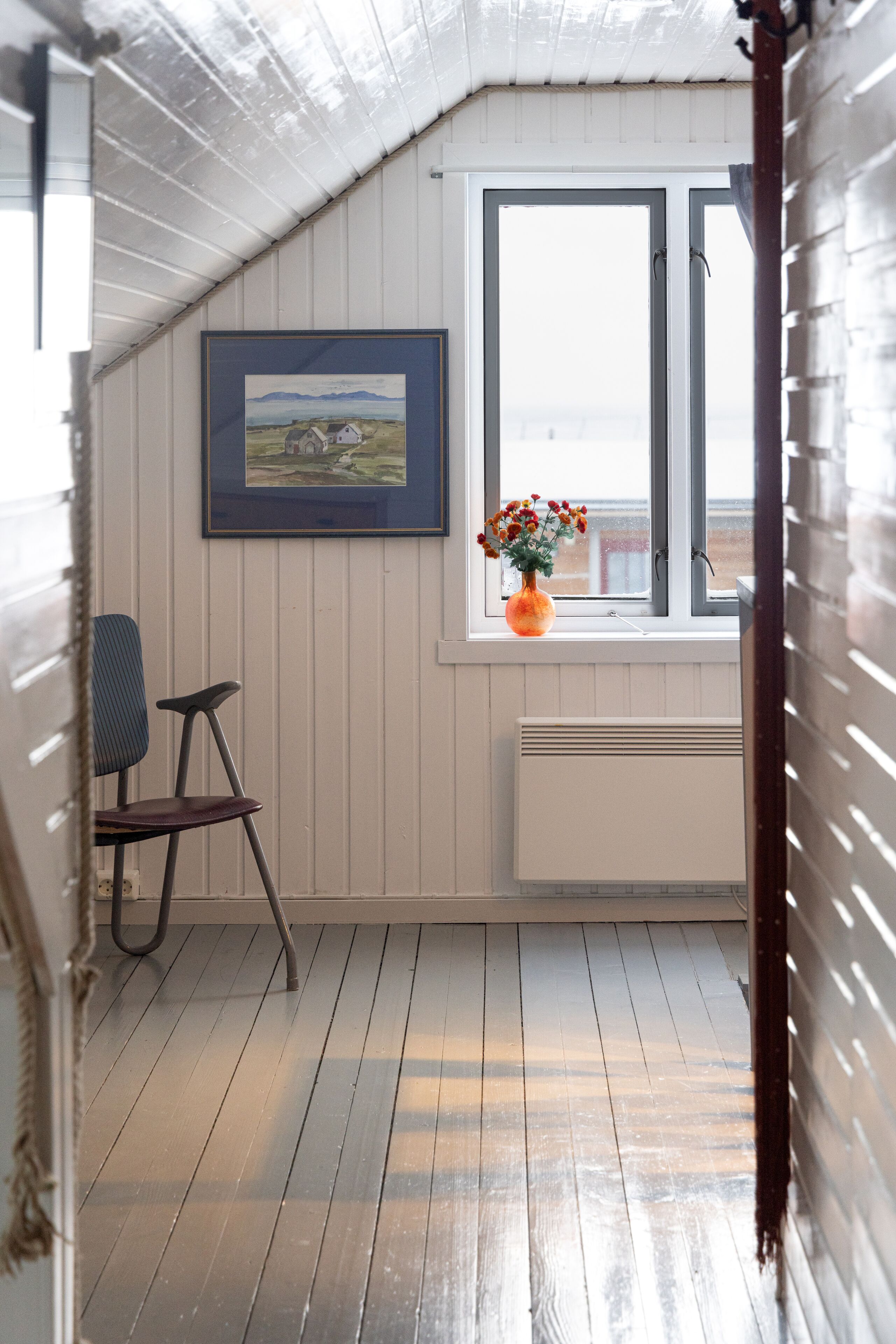 A room with a sloped ceiling, a window with a view, a radiator, and a chair.
