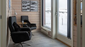 A cozy room with two black armchairs, a small round table, and a large window offering a view of a snowy landscape. - Ekker Island Arctic Lodge (Vadsø)