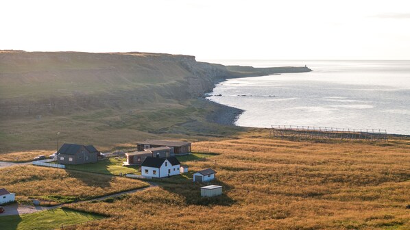 A coastal property with multiple buildings, including a main house and several outbuildings, set against a backdrop of cliffs and the sea.
