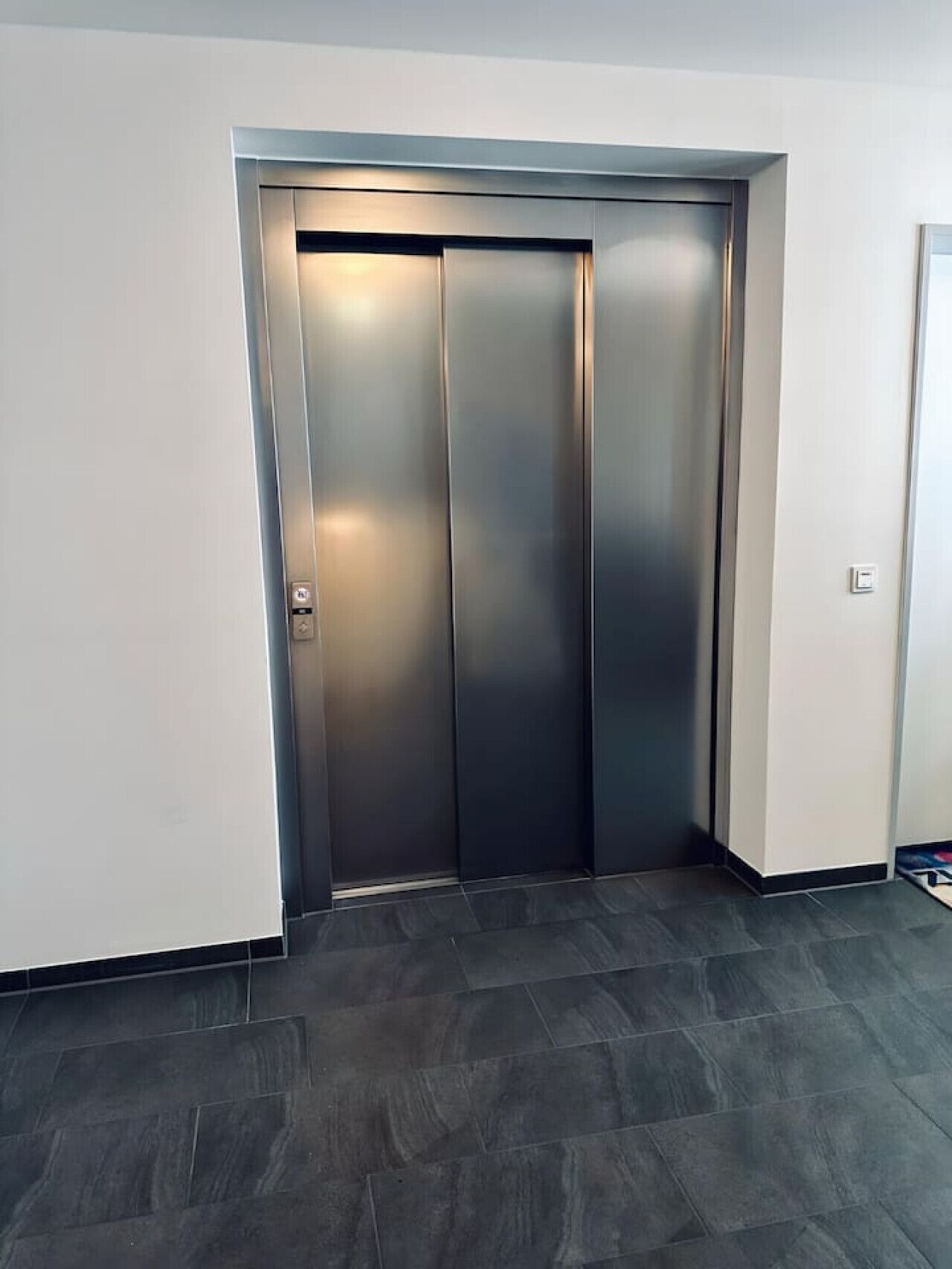 A modern elevator with a metallic finish and a light switch on the wall beside it.