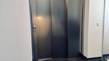 A modern elevator with a metallic finish and a light switch on the wall beside it.