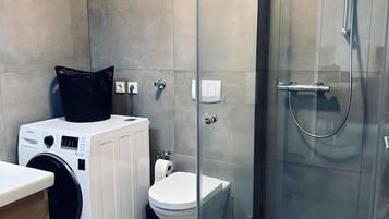 Un bany modern amb dutxa tancada amb vidre, rentamàquina i vàter.