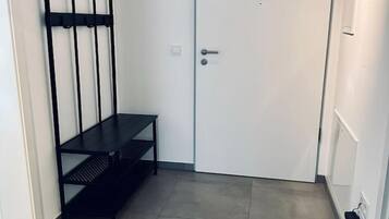 Een hal met een witte deur, een zwarte metalen kapstok en een zwarte bank.