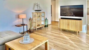 Ein Wohnzimmer mit Couch, Fernseher, Holztisch, Schrank und einem Schiffmodell im Regal.