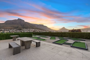 A landscaped outdoor area with a view of a mountain range, benches, and a miniature golf course. - The Hub 602 (Cape Town)