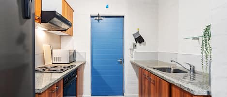 A compact kitchen with wooden cabinets, a blue door, a microwave, and a sink.