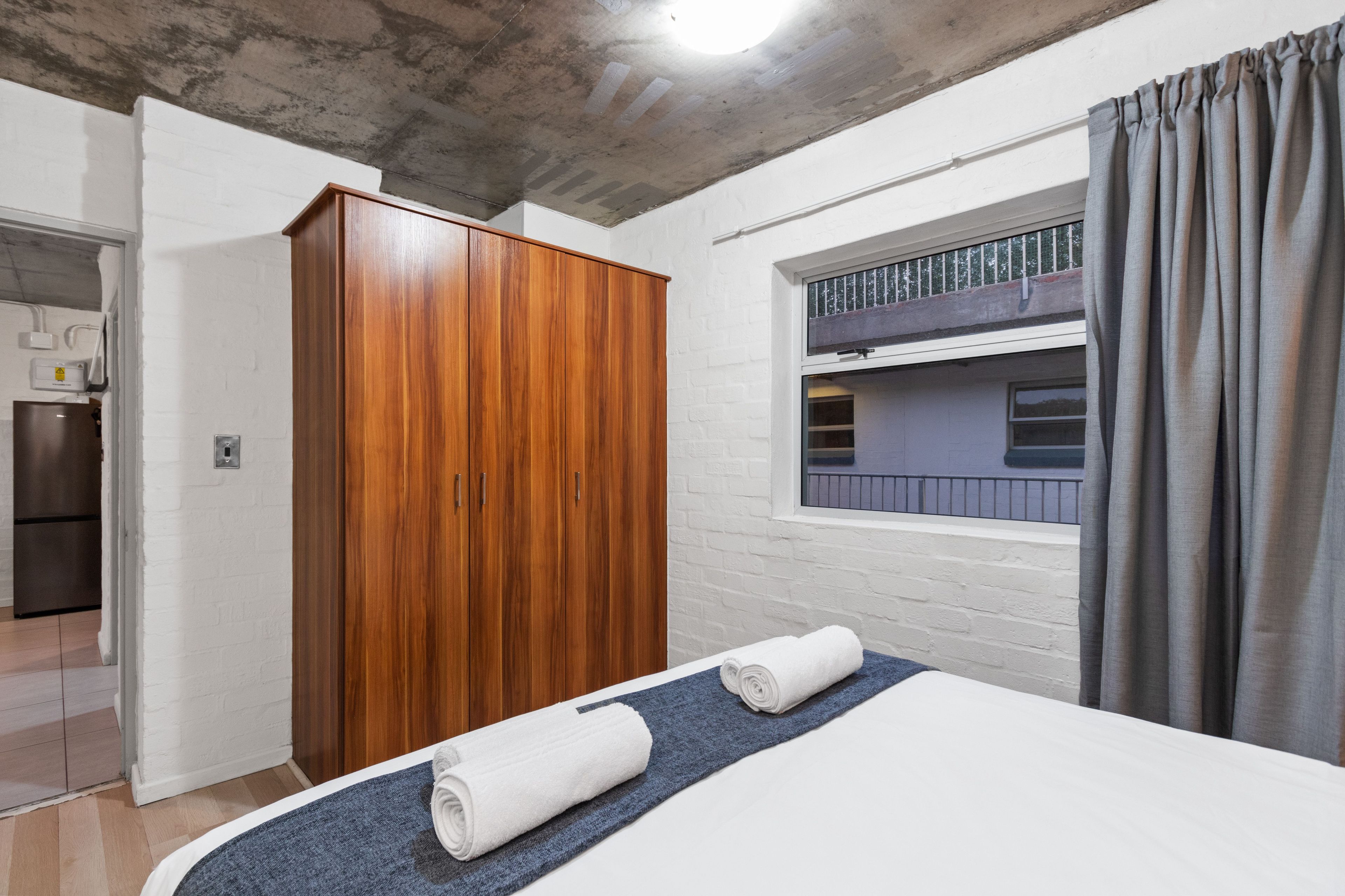 A bedroom with a bunk bed, wooden wardrobe, and a window with curtains.