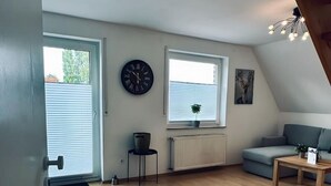 Ein modernes Wohnzimmer mit Holzboden, einem grauen Sofa, einem kleinen Tisch und einer schwarzen Uhr an der Wand.