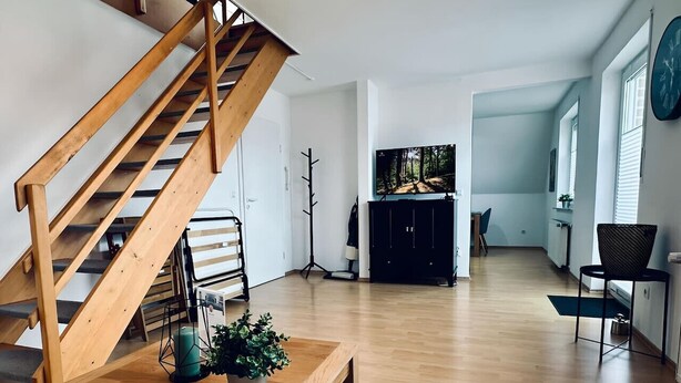 Ein geräumiger Wohnbereich mit einer Holztreppe, einem Flachbildfernseher und einem Esstisch mit einer Topfpflanze.