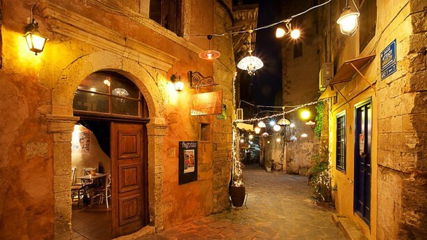 A narrow street with stone buildings, a wooden door, and string lights.