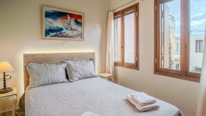 A neatly made bed with a headboard, a bedside table with a lamp, and a window with curtains.