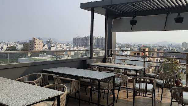 A rooftop terrace with outdoor seating and a view of the cityscape. - Hotel Mewar Shine (Udaipur)