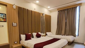A hotel room with a large bed, a wooden headboard, a small seating area, and a window with curtains. - Hotel Mewar Shine (Udaipur)