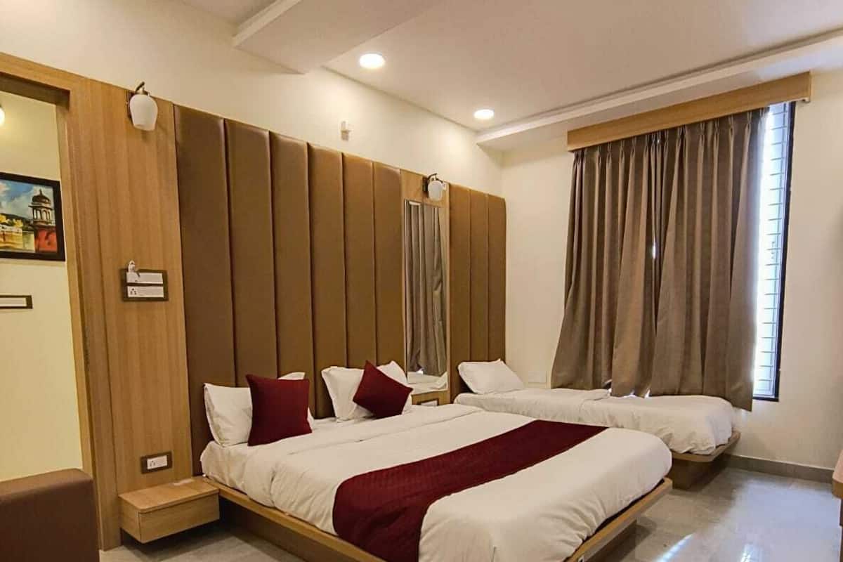 A hotel room with a large bed, a wooden headboard, a small seating area, and a window with curtains.