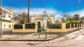 A street view with a building featuring a large archway, a green metal bench, and a palm tree.