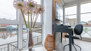 Ein modernes Zimmer mit großem Fenster, Schreibtisch, Stuhl und einer dekorativen Vase mit Blumen.