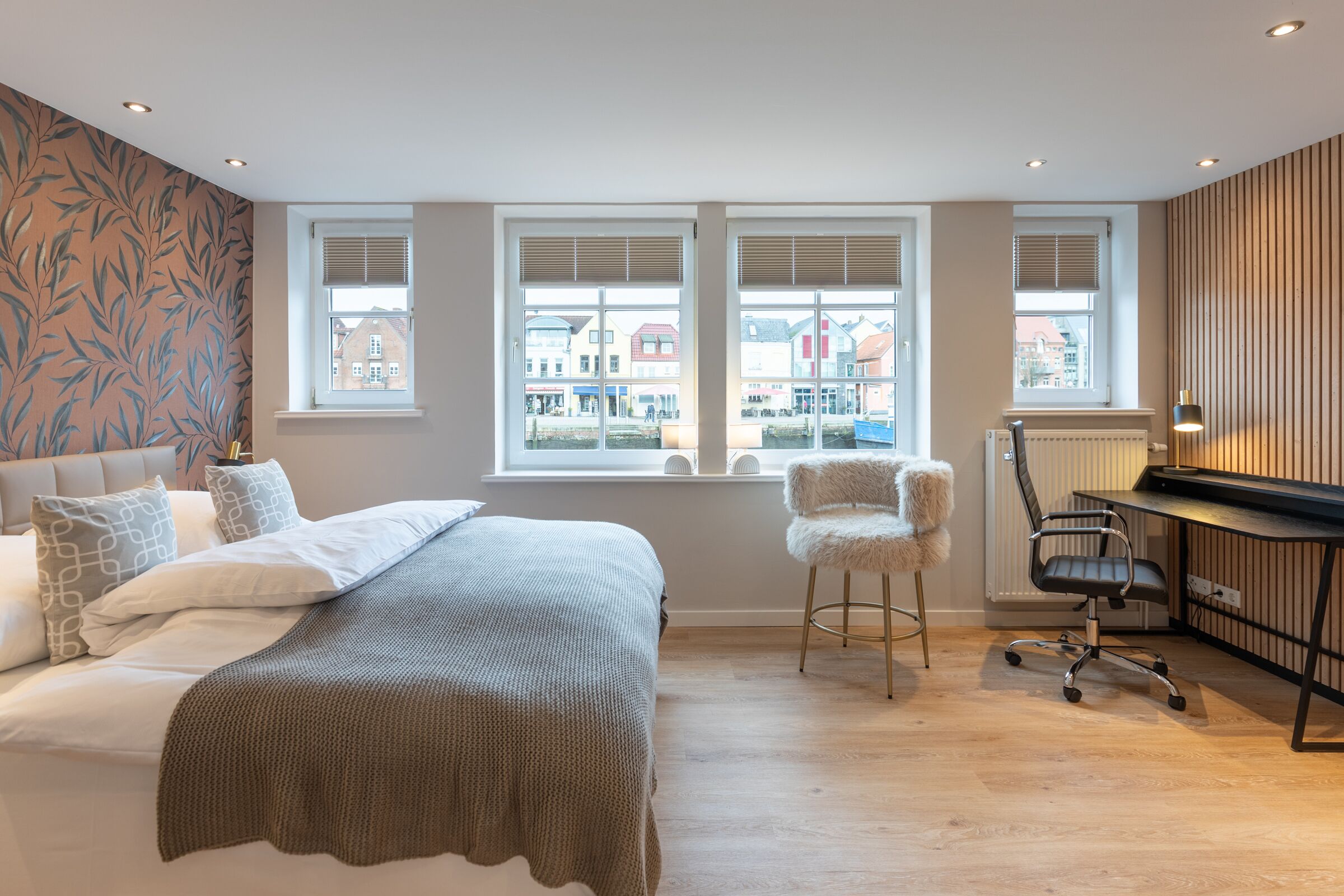 Un dormitorio con cama, dos ventanas, un escritorio y una silla.