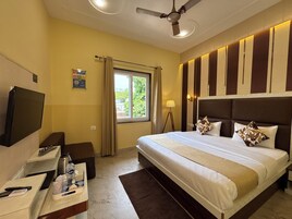 Une chambre d’hôtel avec un lit, un bureau avec une télévision, une lampe et une fenêtre avec des rideaux.