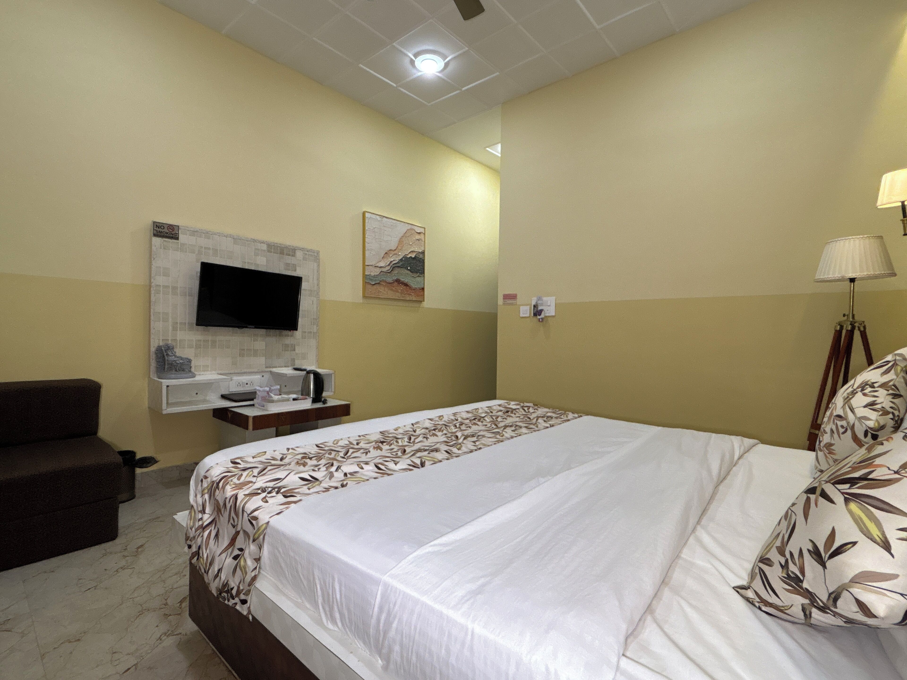 Ein Hotelzimmer mit Bett, Wandfernseher, einem kleinen Tisch mit Wasserkocher und einer Couch.