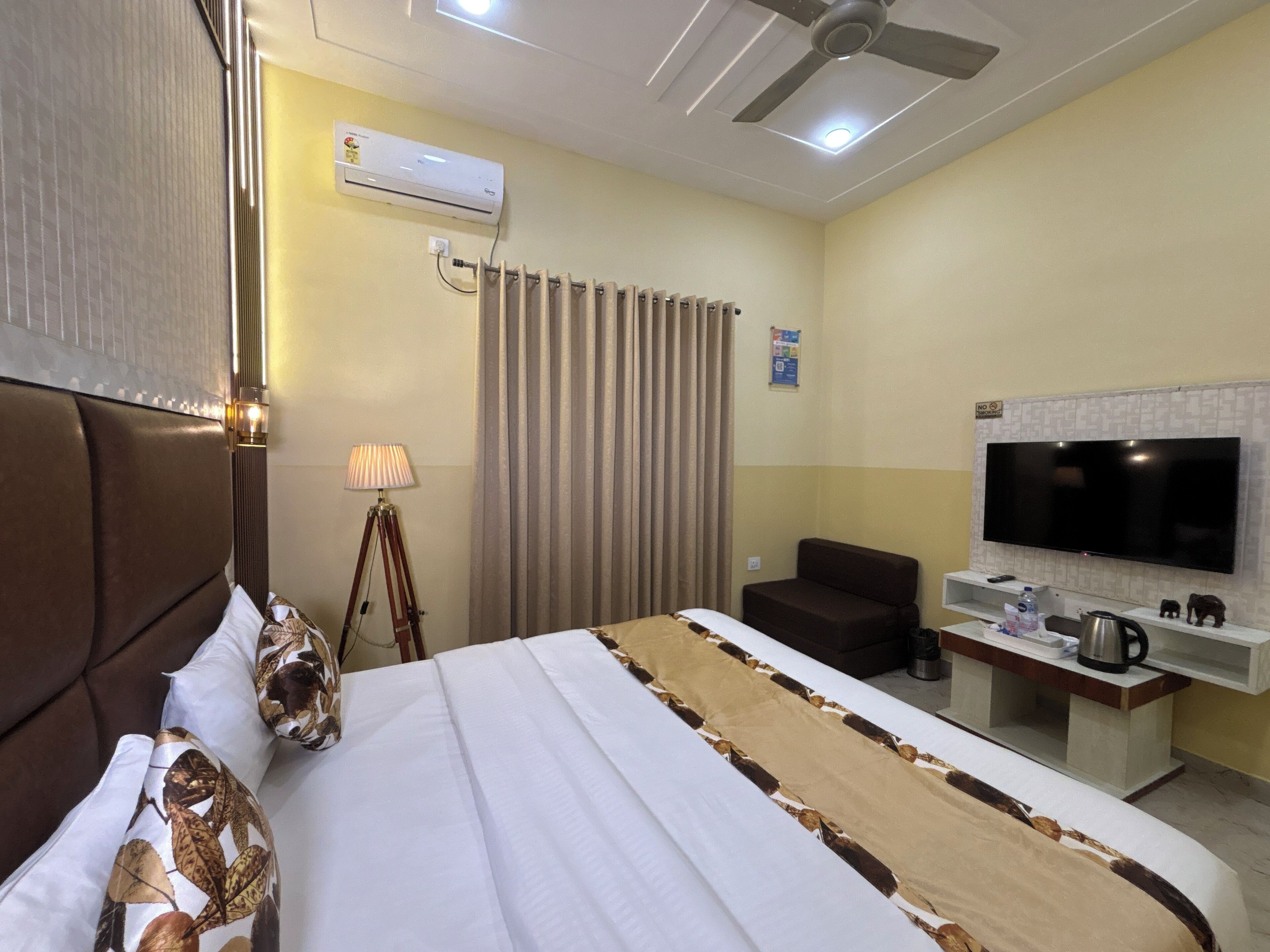 A hotel room with a bed, a desk with a flat-screen TV, a coffee maker, and a wall-mounted air conditioner.