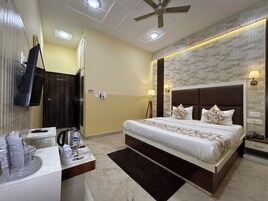 Habitación de hotel con una cama grande, un televisor de pantalla plana en la pared, un escritorio con teléfono y una botella de agua, y un ventilador de techo.