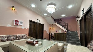 A modern living room with a glass coffee table, a sofa, a staircase, and a chandelier. - The Orchid Retreat Agra - Stay Near Taj Mahal (Agra)