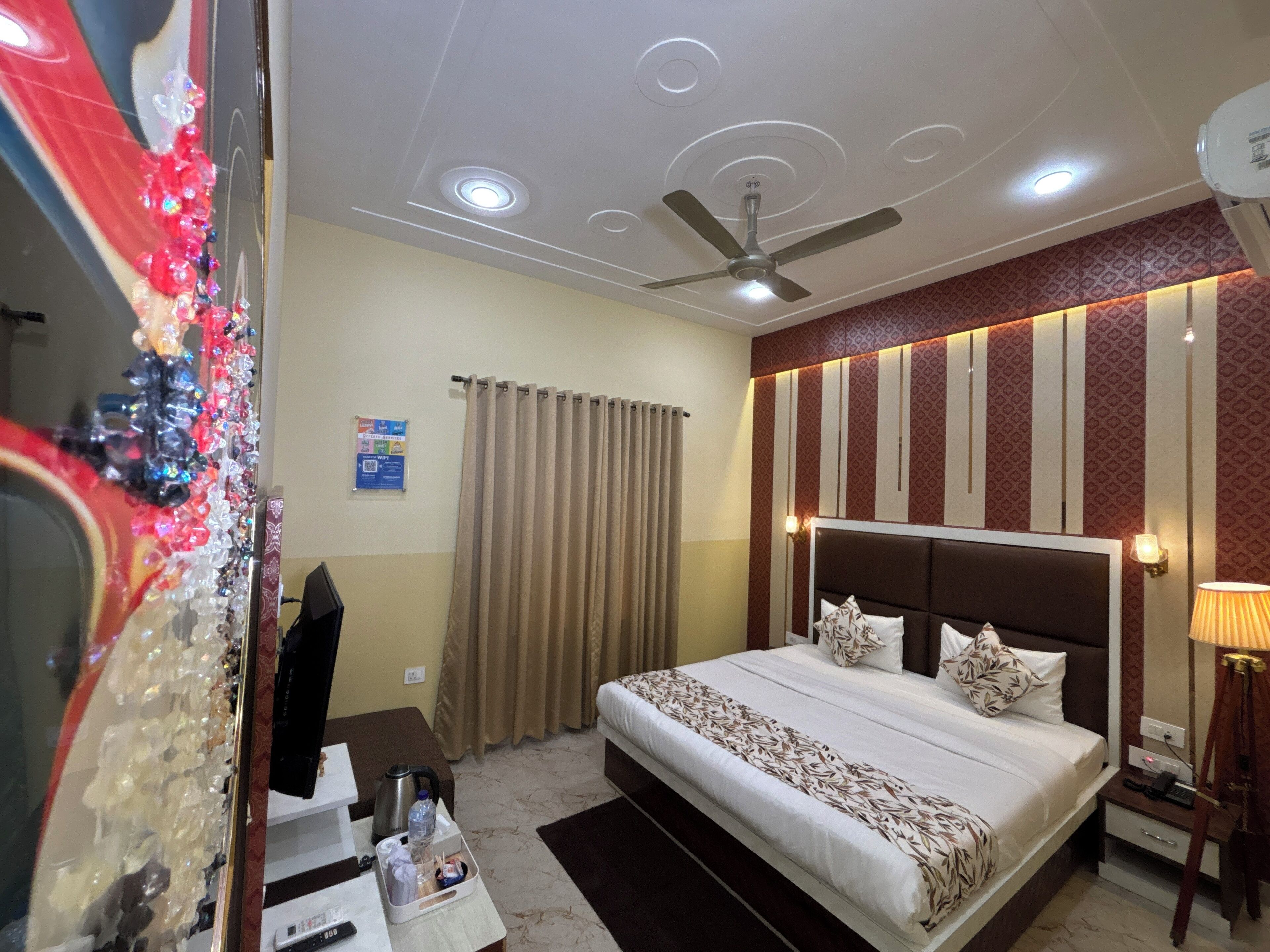 A hotel room with a bed, a ceiling fan, a nightstand, a lamp, and a mirror.