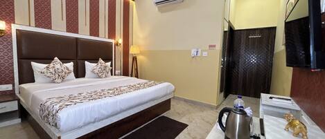 A hotel room with a large bed, a bedside table with a kettle, a TV, and a wardrobe.