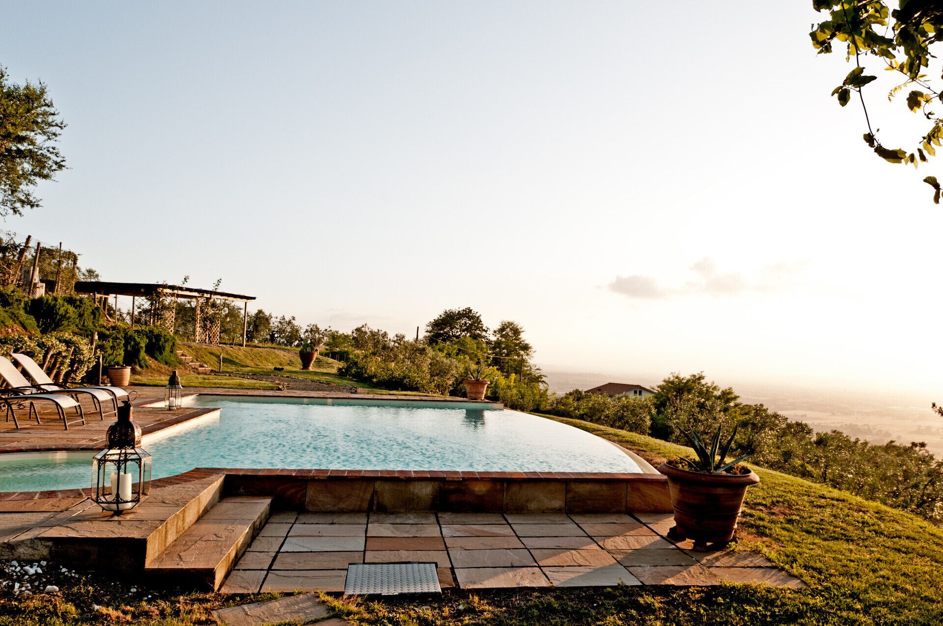 Ein privater Pool mit einer Pergola, Liegestühlen und Kübelpflanzen.