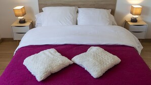 A neatly made bed with white linens, two bedside tables with lamps, and a purple bedspread.