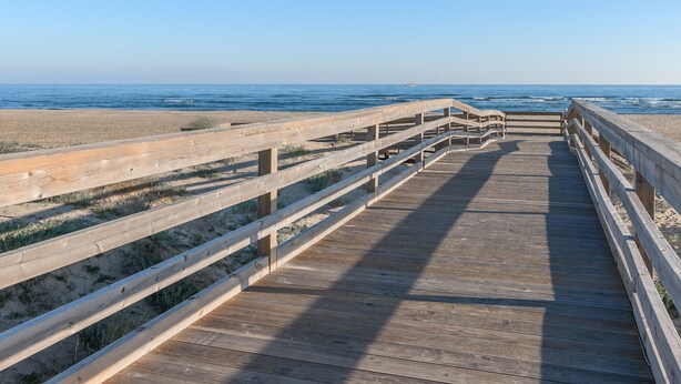 A wooden boardwalk leading to a beach with clear skies.