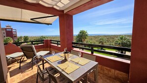A balcony with a table set for two, a bottle of champagne, and a view of the ocean and greenery.