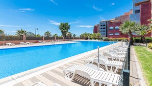 A swimming pool with lounge chairs and palm trees, surrounded by a building with balconies.