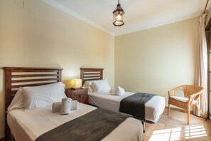 A hotel room with two beds, a nightstand with a lamp, a wicker chair, and a window with curtains. - Las Palmeras - Punta del Moral Beach PLHP51P65 (Punta del Moral)