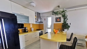A modern kitchen with white cabinets, a black refrigerator, a yellow countertop, and a central island with bar stools. - Mario` place - penthouse with sea view terrace (Dubrovnik)