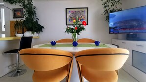 A dining area with a white table, two orange chairs, a vase with flowers, and a TV on the wall. - Mario` place - penthouse with sea view terrace (Dubrovnik)