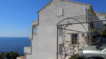 A building with a balcony, a view of the sea, and a parked car.