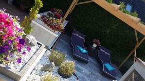 Een terras met twee lounge fauteuils, genaamd "Lieblingsplatz", omringd door sierplanten en een pergola.