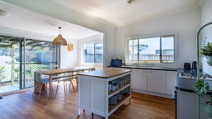 A modern kitchen with a dining area, large windows, and a view of the outdoors. - Beachside Cottage - Cudmirrah (Cudmirrah)