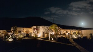 Edifício de pedra com um pátio iluminado por iluminação ambiente, rodeado por cactos e plantas do deserto.