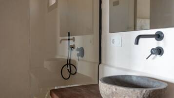 A bathroom with a stone sink, a mirror, a shower, and a wooden countertop.