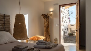 Quarto com uma cama grande, luminária pendente, escultura de madeira e vista para o exterior.