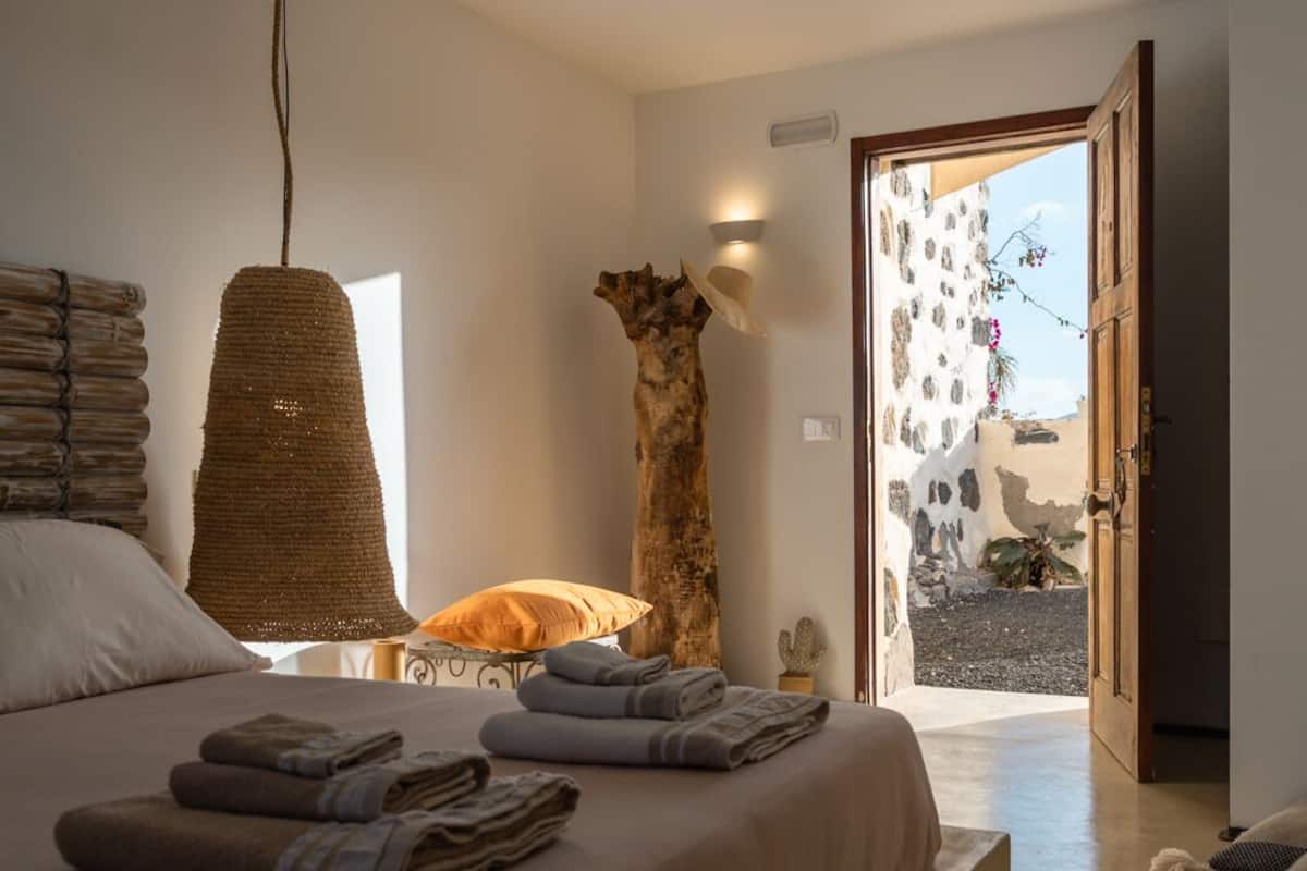 Un dormitorio con una cama grande, un lámpara colgante, una escultura de madera y vistas al exterior.