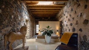 Um interior rústico com paredes de pedra, uma escultura de cavalo de madeira, uma grande planta em vaso e um sofá de couro.