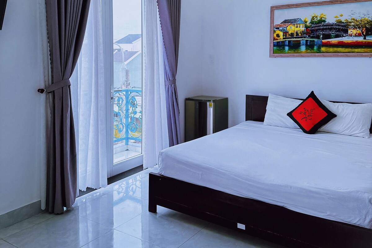 A modern hotel room with a large bed, a painting on the wall, and a balcony with curtains.